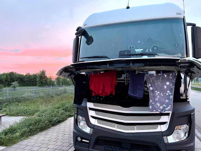 Ein Lkw steht mit offener kühlerklappe auf einem Parkplatz, an dieser Klappe hängt Wäsche zum trocknen. 