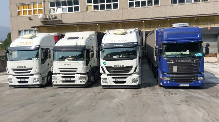 lkw stehen an einer rampe und warten auf die beladung. zu sehen sind drei weiße iveco und ein blauer scania.