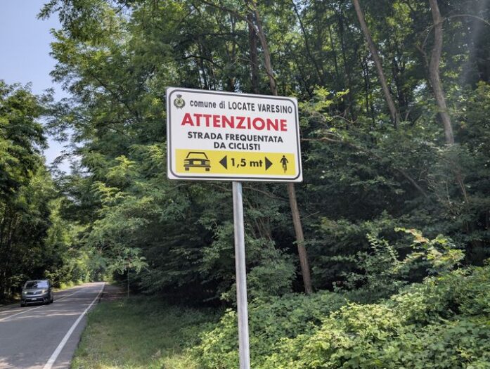 bild zeigt ein schild, auf welchem auf italienisch um abstand beim überholen von fahrradfahrern gebeten wird