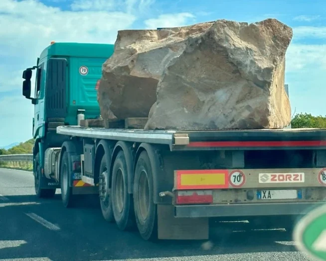 Das Bild zeigt einen Lkw von nah mit einem Felsbrocken, der ungesichert auf der Ladefläche liegt