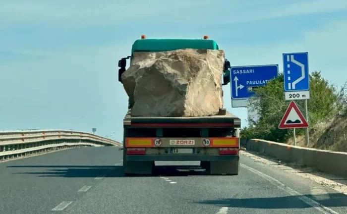 Das Bild zeigt einen Lkw auf Sardinien mit einem Felsbrocken, der ungesichert auf der Ladefläche liegt